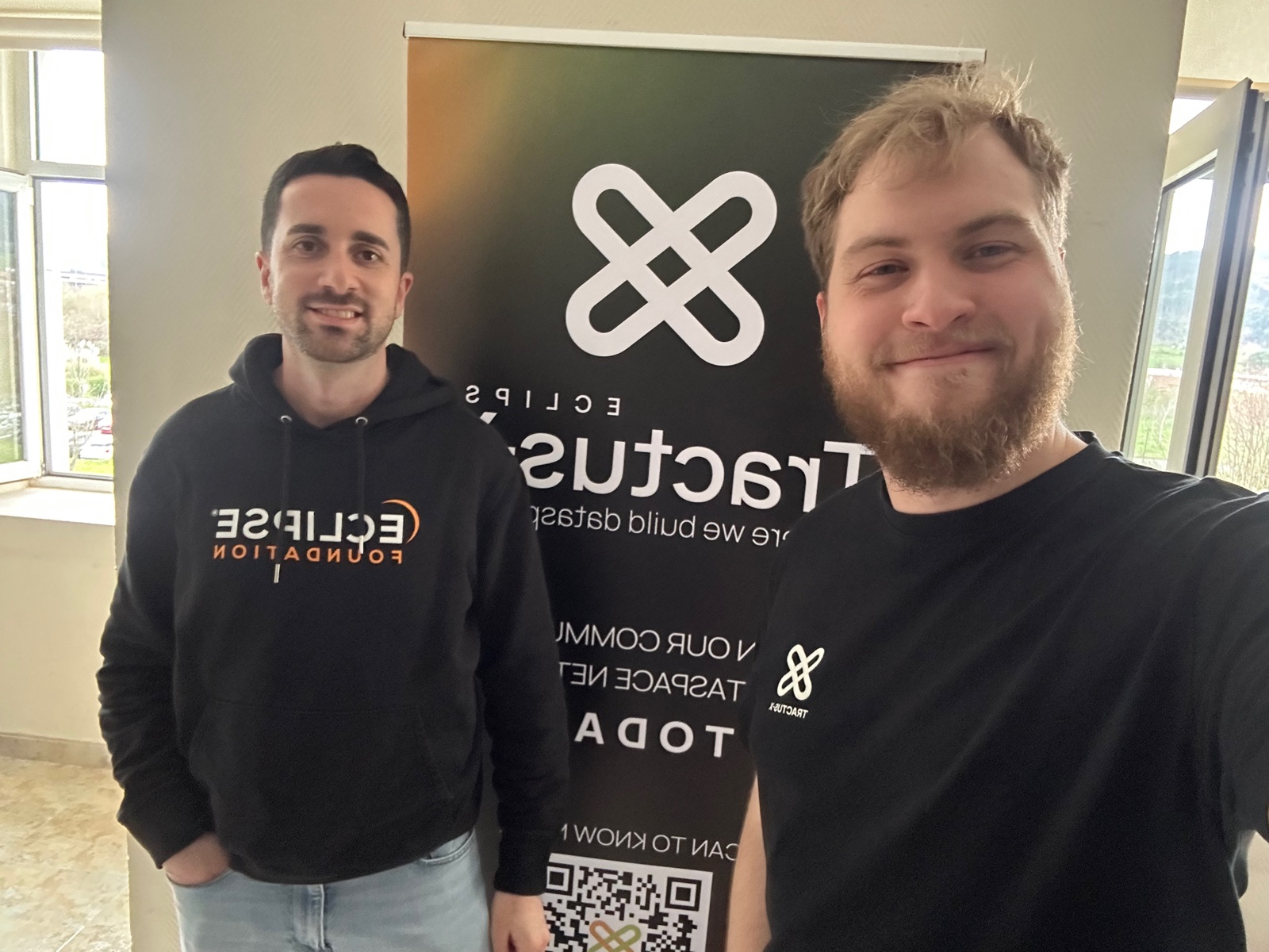 Two participants smiling in front of the Eclipse Tractus-X roll-up banner