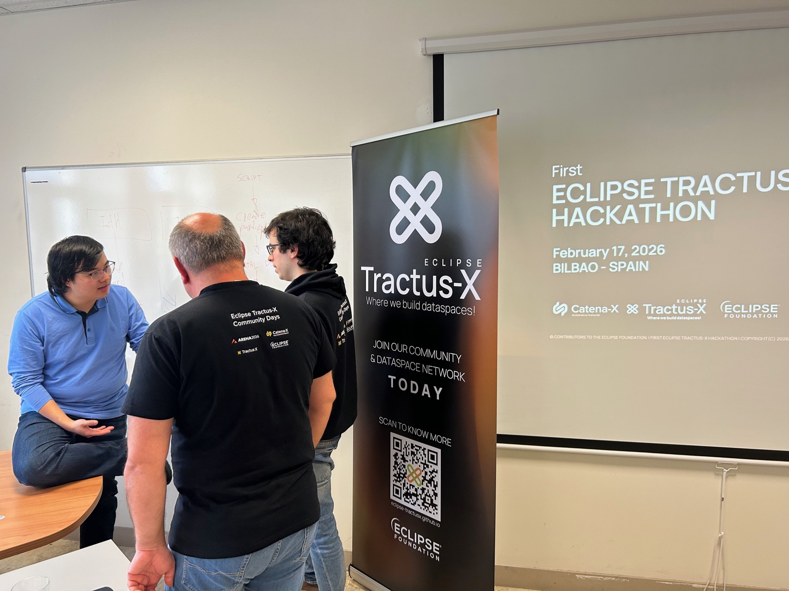 Three participants discussing an architecture sketch on a whiteboard next to the Tractus-X banner